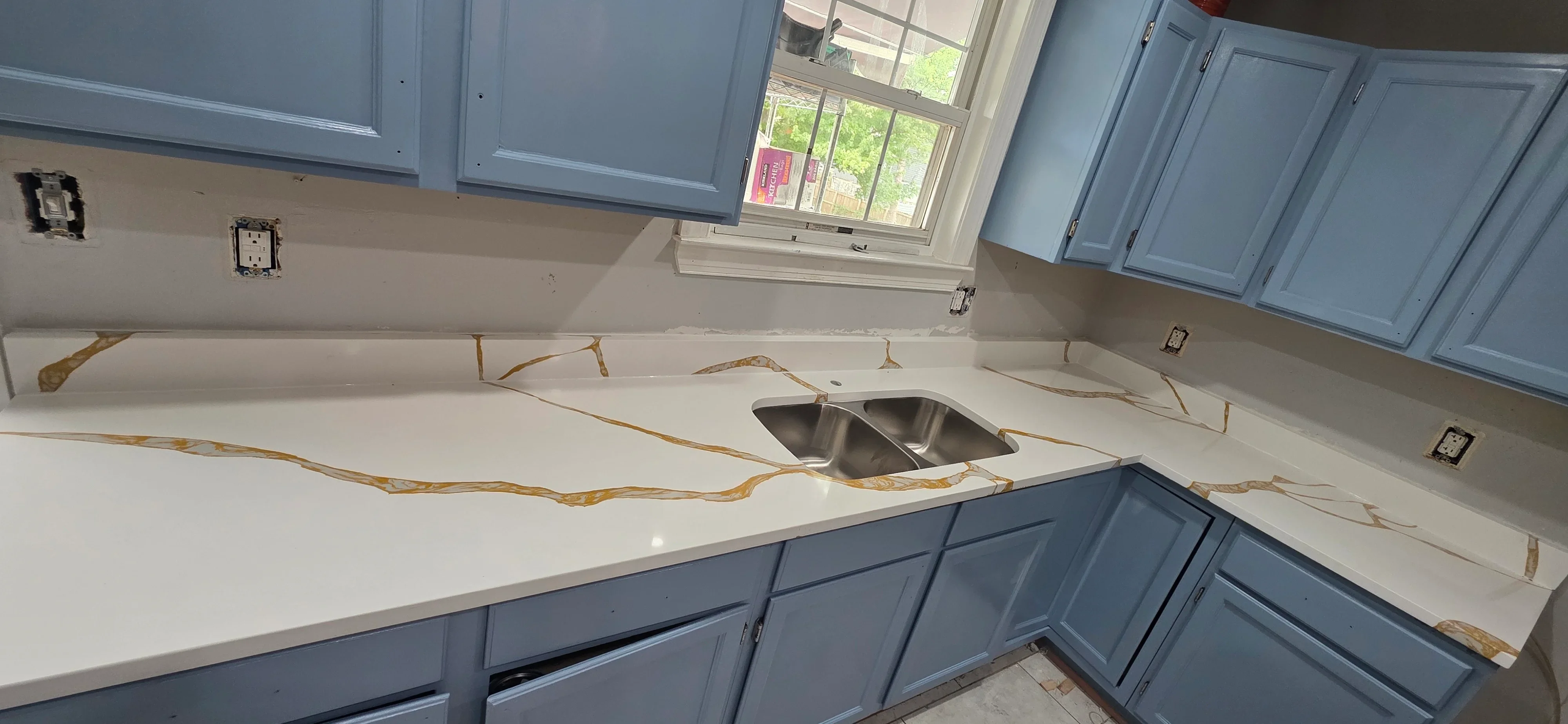 White quartz countertop with gold veining and stainless steel sink cutout in kitchen remodel