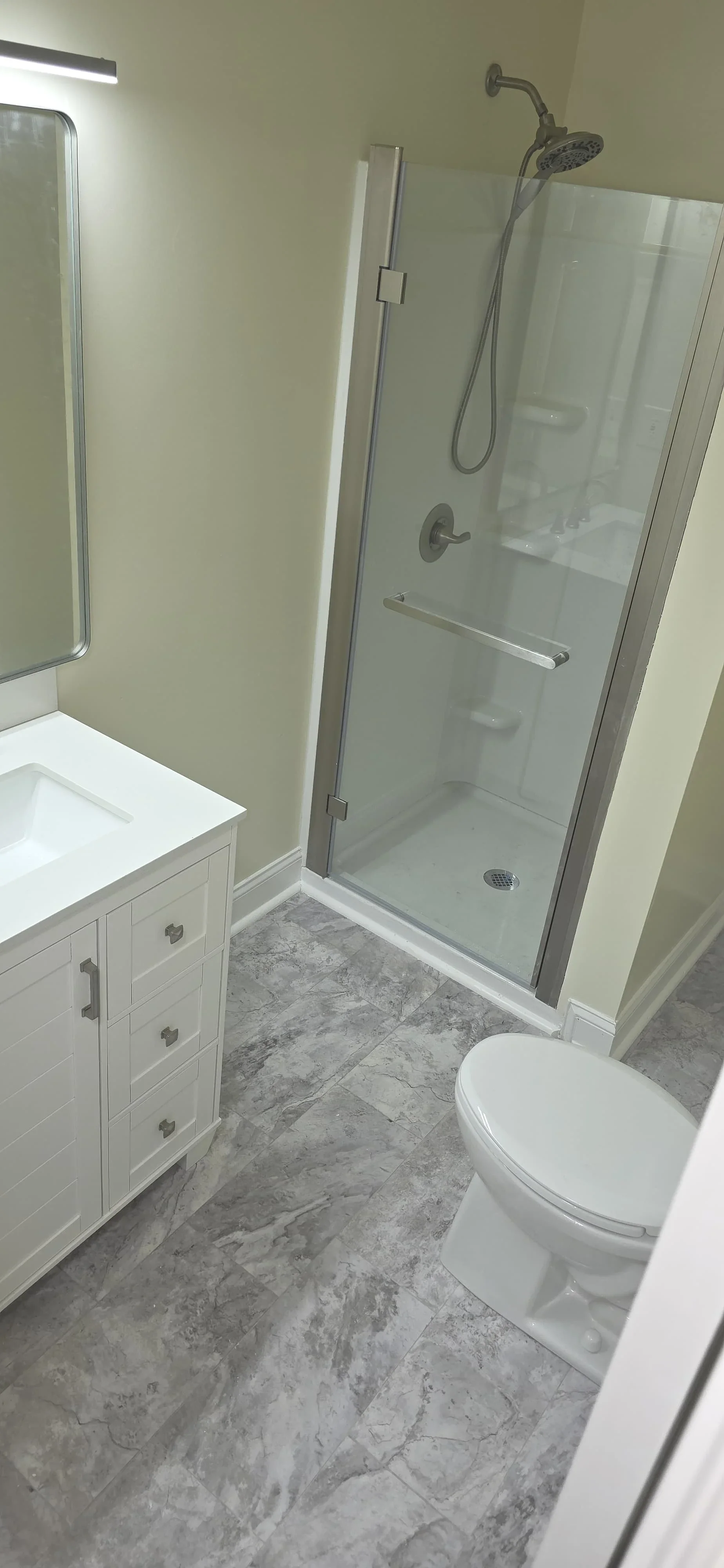 Modern bathroom with frameless glass shower, white vanity, and gray marble tile flooring